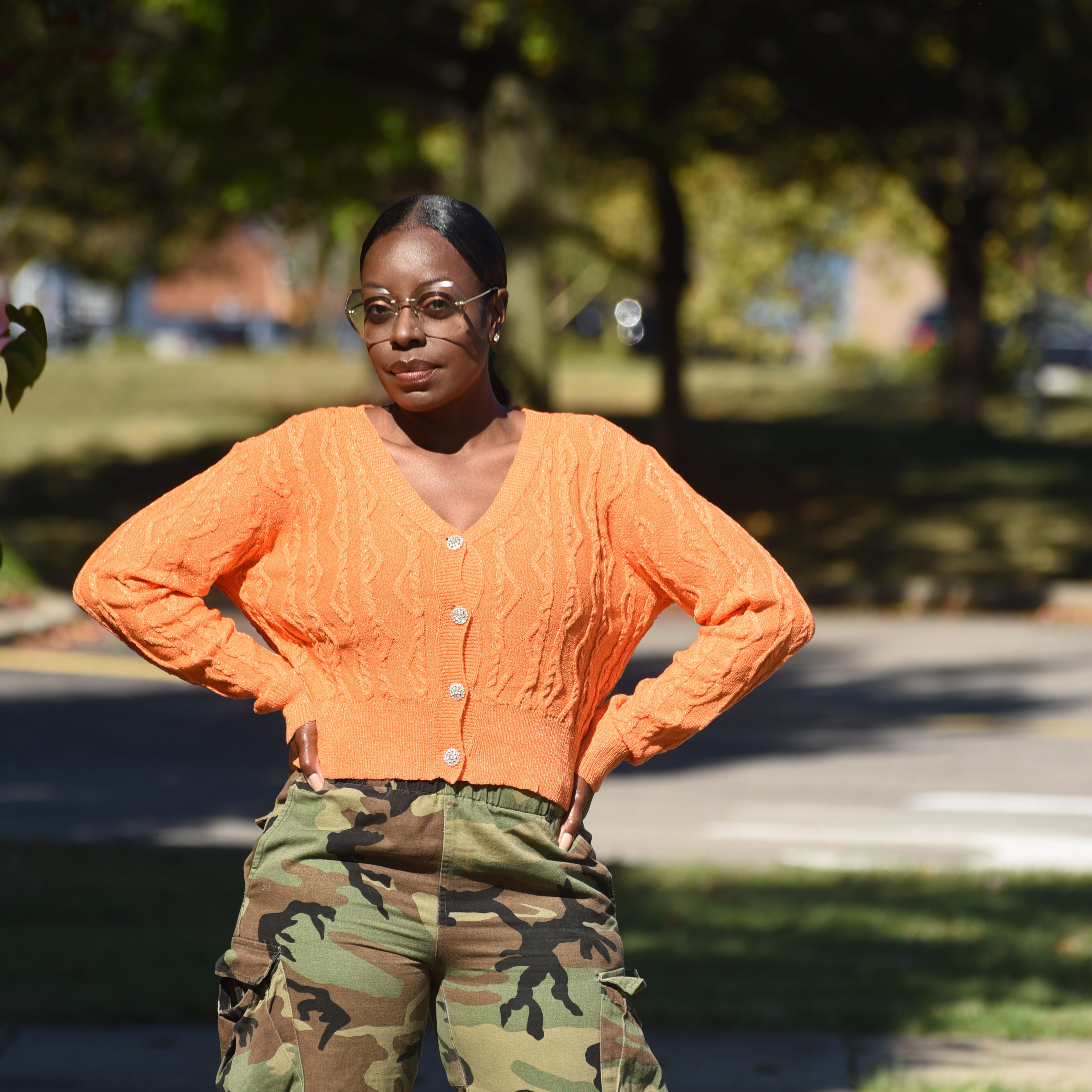 Person wearing an orange jacket and camouflage shorts standing outdoors with a blurred background