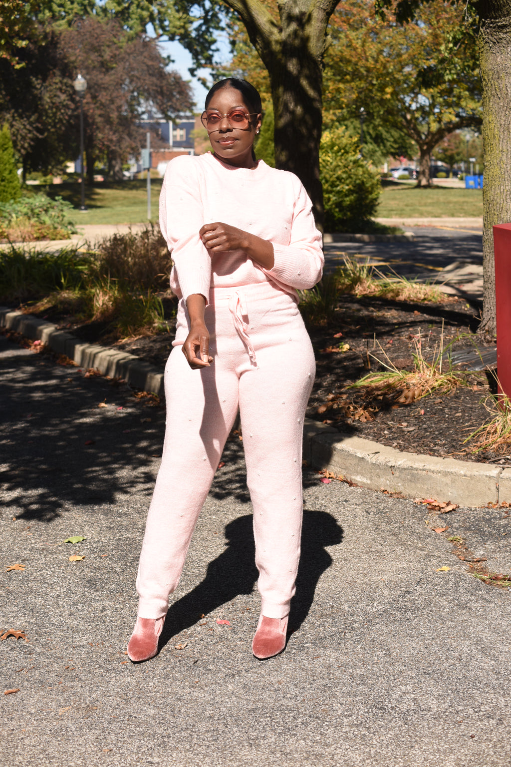 Person in a pink pearl outfit standing on a road with trees and grass in the background